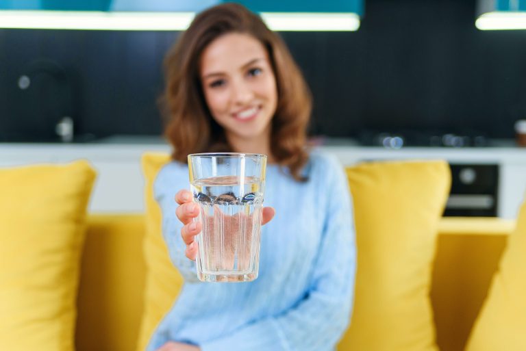 אישה מחייכת ומחזיקה כוס מים ממתקן